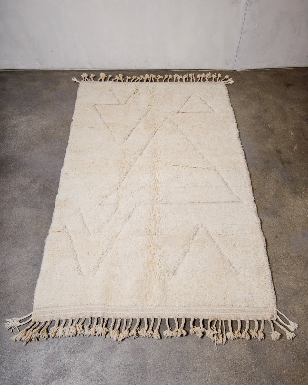 Cream wool rug with design woven in natural wool laying flat on concrete floor.